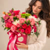 Woman holding a pink hatbox arrangement of roses and mixed blooms