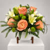 Peach roses and white lilies arranged in a white vase