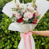 Bouquet of pink and red flowers wrapped in white paper with a pink ribbon