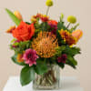 Mixed bouquet in a square glass vase with orange, pink, and yellow blooms