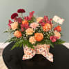 Mixed bouquet of orange and pink flowers in a floral box with a ribbon