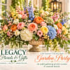 Large mixed floral arrangement in a decorative urn with pink, blue, yellow, and white blooms.