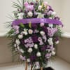 Standing floral spray with white and lavender flowers and a purple ribbon banner