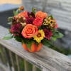Orange and burgundy flower arrangement in a pumpkin container