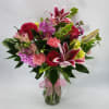 Mixed bouquet of pink and red flowers in a glass vase with a pink ribbon