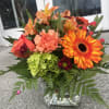 Mixed bouquet in a clear glass vase with orange and coral blooms