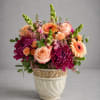 Mixed bouquet of peach, pink, and purple flowers in a decorative ceramic pot