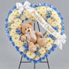 Heart-shaped floral wreath with a teddy bear and ribbon on a stand