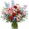 Bouquet of red and pink roses with lilies and blue flowers in a glass vase