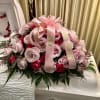Pink and red rose arrangement on a white casket with a pink ribbon.