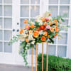 Large orange and pink floral arrangement on a gold stand