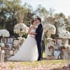 Bride and groom standing among large white and blush floral arrangements outdoors