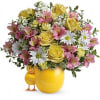 Yellow roses and pink flowers arranged in a yellow vase with a small chick figurine