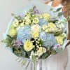 Bouquet of pale roses, blue hydrangeas, and lavender flowers wrapped in light blue paper