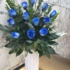 Blue roses in a tall white vase with mixed greenery