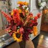 Tall autumn floral arrangement in a dark vase with orange and red blooms