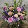 Mixed pink, purple, and peach flowers arranged in a glass vase