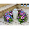 Floral wreath with pink roses and purple-blue blooms around a white urn