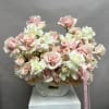 Pink and white roses arranged in a white vase with a pink ribbon