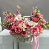 Pink roses and white orchids arranged in a white basket with a ribbon