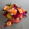 Floral arrangement in a pumpkin-shaped container with roses and gerbera daisies