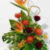 Tall tropical arrangement with bird of paradise, red roses, orange protea and yellow blooms on large glossy leaves