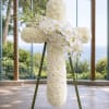 White floral cross on an easel with orchids and clustered blooms