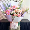 Handheld bouquet of pink and white flowers wrapped in lavender paper