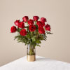 Red roses arranged in a clear glass vase with greenery