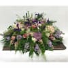 Large mixed floral arrangement with purple, pink, and white blooms on a casket