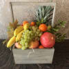 Wooden crate filled with assorted fruit including bananas, grapes, oranges, and pomegranates