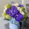 Bouquet of purple orchids, white roses, and blue hydrangeas in a white hat box