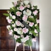 Large pink and white funeral wreath on an easel with a black ribbon