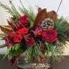Red roses in a glass vase with burgundy ribbon and pinecones
