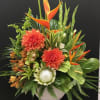 Tropical floral arrangement with orange blooms in a white vase