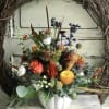 Mixed floral arrangement in a white pumpkin-shaped vase with orange, yellow, and purple blooms