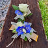 Two floral corsages with white roses and blue flowers on a wooden surface