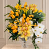 Yellow roses and orchids arranged in a clear glass vase