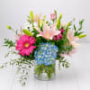Mixed bouquet with pink lilies, blue hydrangea, and a pink gerbera daisy in a glass vase