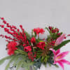 Holiday arrangement with red flowers, berries, a pink lily, and evergreen branches in a white vase