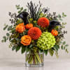 Orange and black floral arrangement in a clear glass vase with pumpkins
