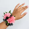 Pink carnation wrist corsage with black ribbon on a hand