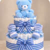 Blue teddy bear atop a diaper cake with striped ribbons and baby booties