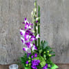 Purple orchids in a green square vase with a small glass candle holder