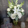 White floral arrangement in a glass vase with roses, lilies, and hydrangeas