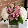 Pink roses and orchids arranged with white hydrangeas in a glass vase