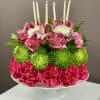 Pink and green floral centerpiece with white candles on a pedestal stand