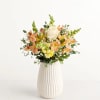 Mixed bouquet of peach and yellow flowers in a white vase