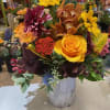 Mixed bouquet with yellow roses, sunflowers, and orchids in a white vase