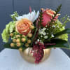 Peach and pink roses arranged in a gold pumpkin vase
